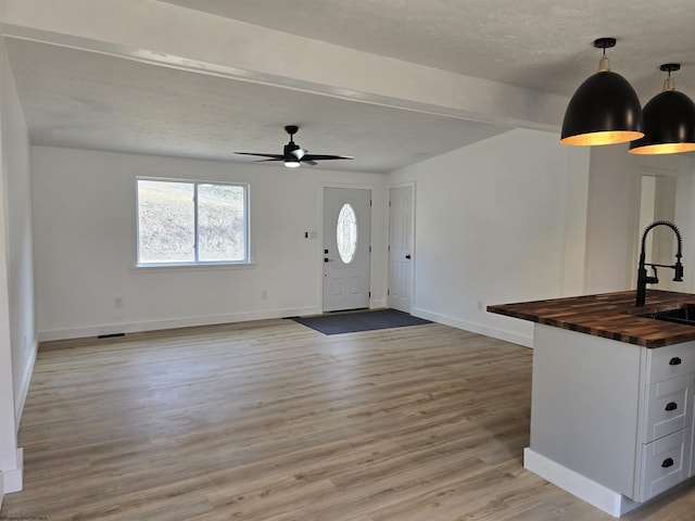 foyer entrance with light wood-style flooring, baseboards, ceiling fan, and a textured ceiling