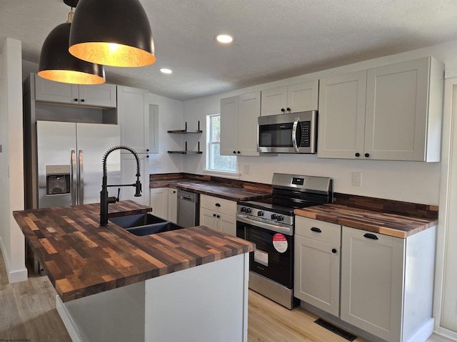 kitchen featuring stainless steel appliances, butcher block counters, a sink, visible vents, and open shelves