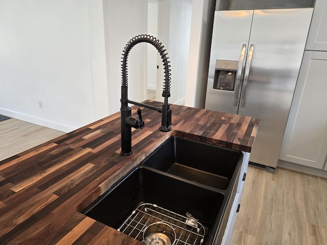 room details with light wood finished floors, wooden counters, a sink, stainless steel fridge, and baseboards