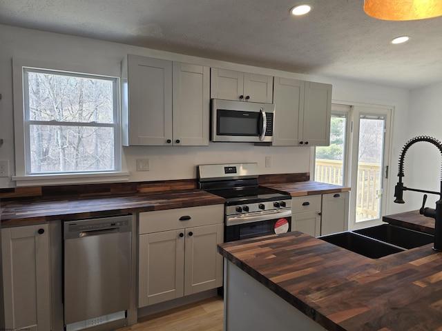 kitchen with a textured ceiling, a sink, wooden counters, appliances with stainless steel finishes, and light wood-type flooring