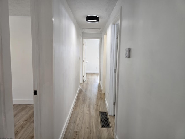 hall featuring visible vents, light wood-style flooring, attic access, a textured ceiling, and baseboards