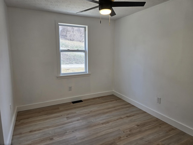 empty room featuring baseboards, visible vents, a ceiling fan, wood finished floors, and a textured ceiling