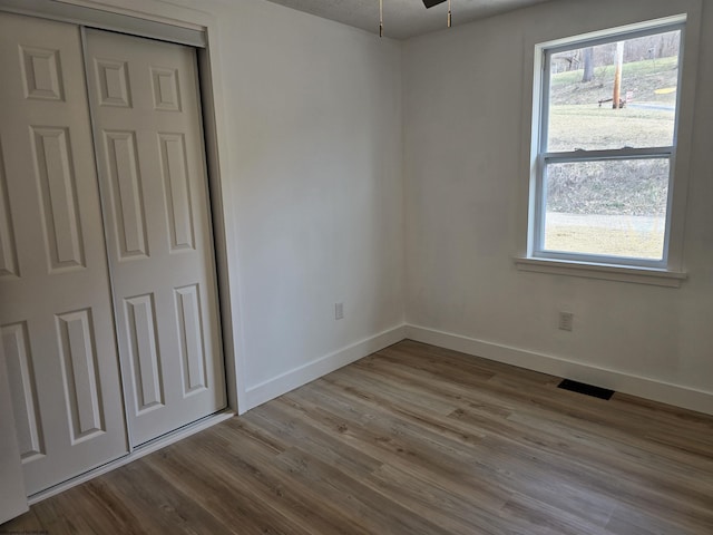 unfurnished bedroom with a closet, wood finished floors, visible vents, and baseboards