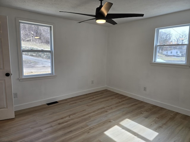 empty room featuring baseboards, visible vents, light wood-style flooring, and a textured ceiling