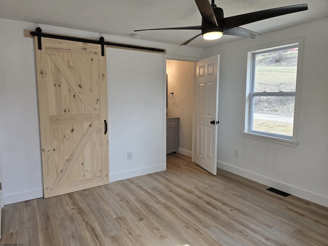 unfurnished bedroom featuring a barn door, light wood-style flooring, visible vents, and baseboards