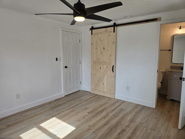 unfurnished bedroom featuring ensuite bath, light wood-style flooring, baseboards, and a barn door