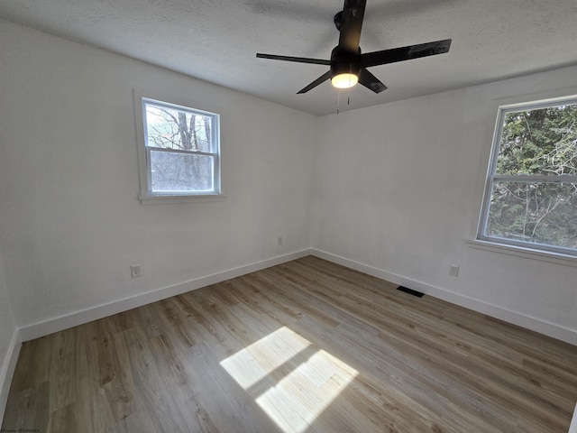 empty room featuring a textured ceiling, ceiling fan, visible vents, baseboards, and light wood-type flooring