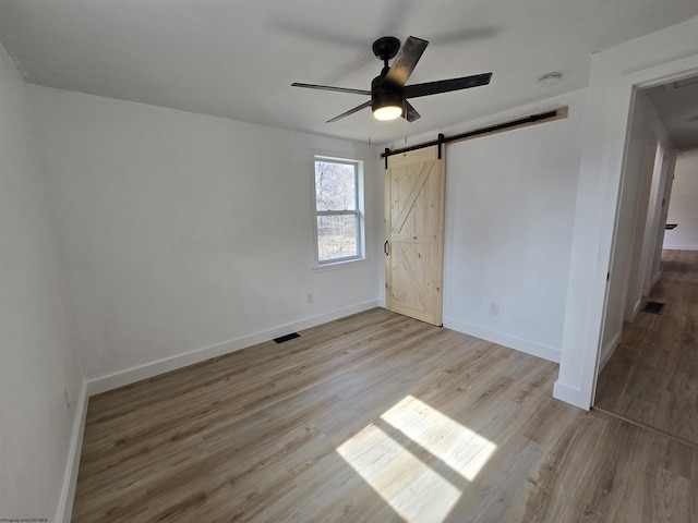 unfurnished bedroom featuring a barn door, visible vents, and wood finished floors