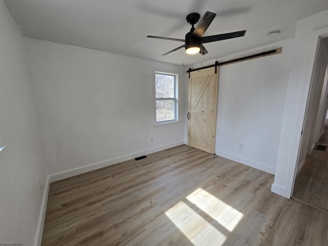 unfurnished bedroom featuring ceiling fan, a barn door, wood finished floors, visible vents, and baseboards