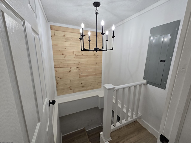 stairway with electric panel, wooden walls, an inviting chandelier, and wood finished floors