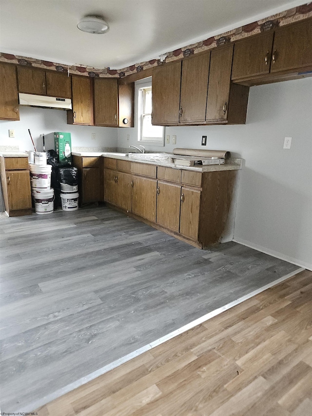 kitchen with light wood-style floors, light countertops, under cabinet range hood, and baseboards