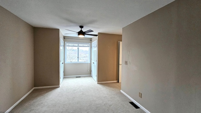 empty room featuring light colored carpet, visible vents, a ceiling fan, a textured ceiling, and baseboards