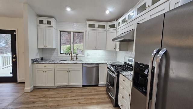 kitchen with appliances with stainless steel finishes, a sink, light stone countertops, and under cabinet range hood