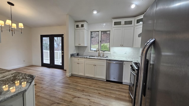 kitchen featuring light stone counters, stainless steel appliances, a sink, white cabinets, and backsplash