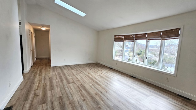 empty room with a skylight, visible vents, wood finished floors, high vaulted ceiling, and baseboards