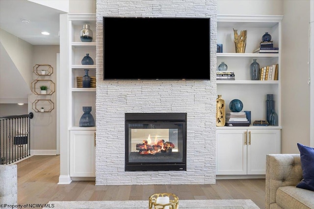 living area featuring a stone fireplace, built in features, and light wood-style floors