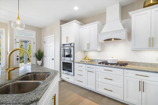 kitchen with appliances with stainless steel finishes, decorative backsplash, a sink, and custom range hood