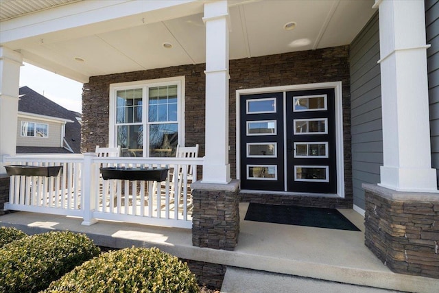 doorway to property featuring a porch and stone siding