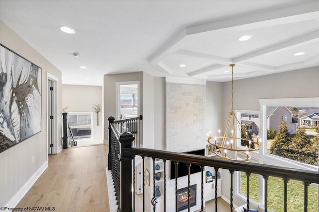 hallway with an inviting chandelier, light wood finished floors, a wealth of natural light, and an upstairs landing