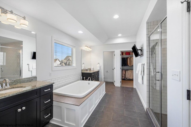 full bath featuring a tub to relax in, a sink, a shower stall, two vanities, and recessed lighting