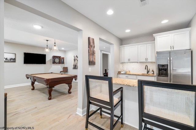 kitchen with light wood finished floors, tasteful backsplash, white cabinets, a sink, and stainless steel fridge