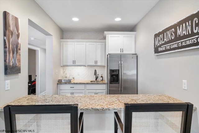 kitchen featuring tasteful backsplash, stainless steel refrigerator with ice dispenser, a sink, and white cabinetry