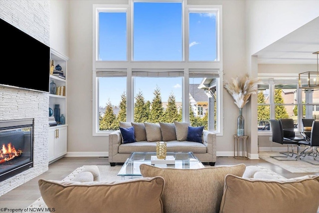 living area featuring a towering ceiling, light wood-style floors, a stone fireplace, a chandelier, and baseboards