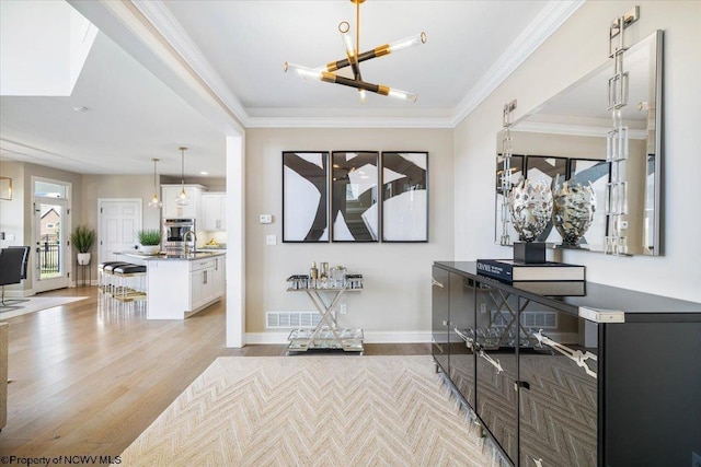 foyer featuring light wood finished floors, a notable chandelier, baseboards, and crown molding