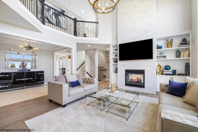 living room with a stone fireplace, a notable chandelier, wood finished floors, built in features, and crown molding