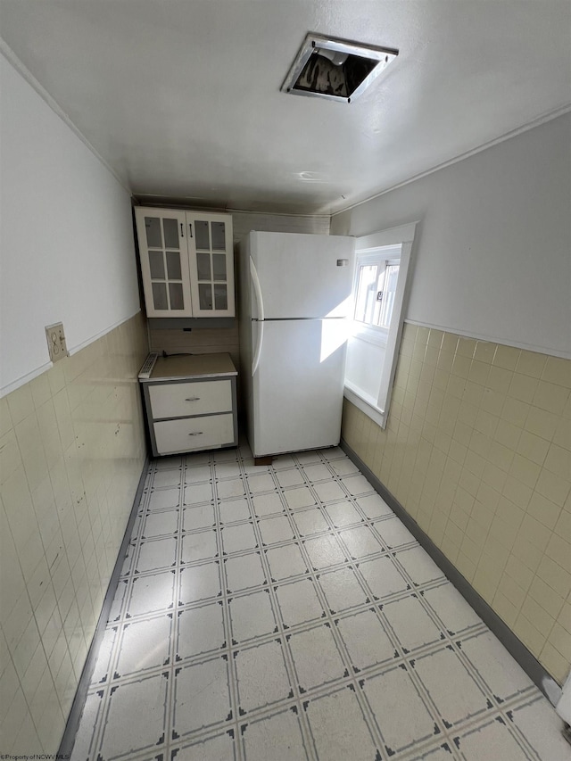 kitchen with tile walls, wainscoting, freestanding refrigerator, light floors, and glass insert cabinets