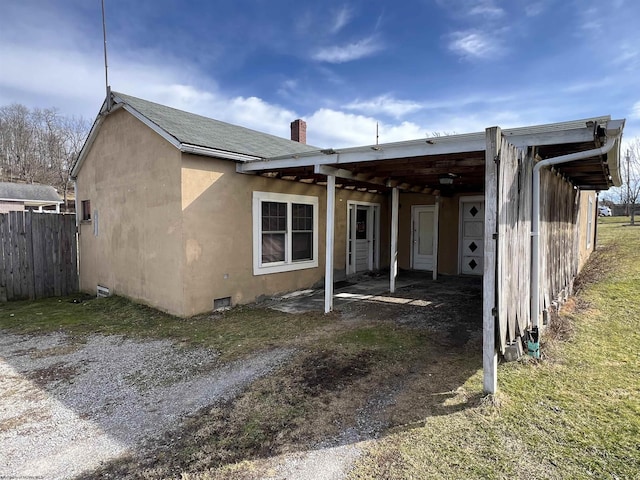 rear view of house with a shingled roof, crawl space, fence, and stucco siding