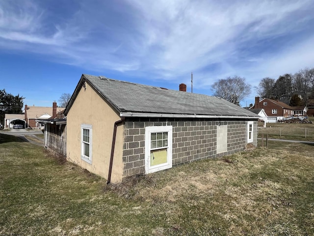 exterior space featuring a lawn, a chimney, concrete block siding, roof with shingles, and stucco siding