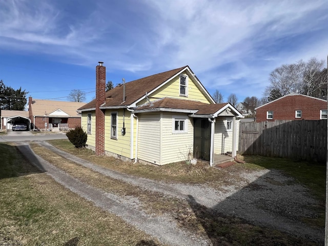 rear view of property featuring a chimney, fence, and roof with shingles