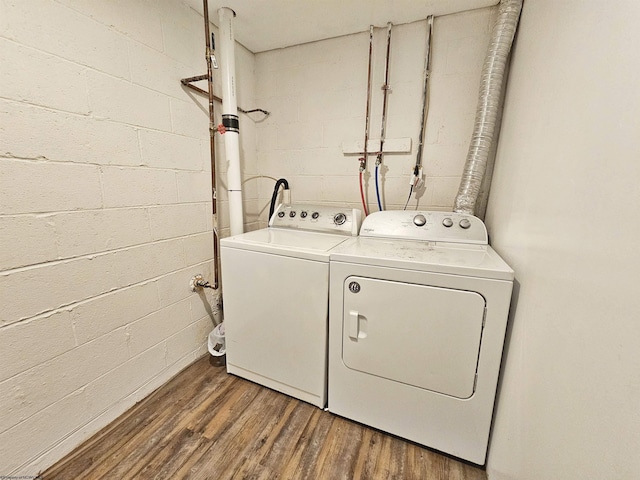 washroom featuring concrete block wall, laundry area, washer and clothes dryer, and wood finished floors