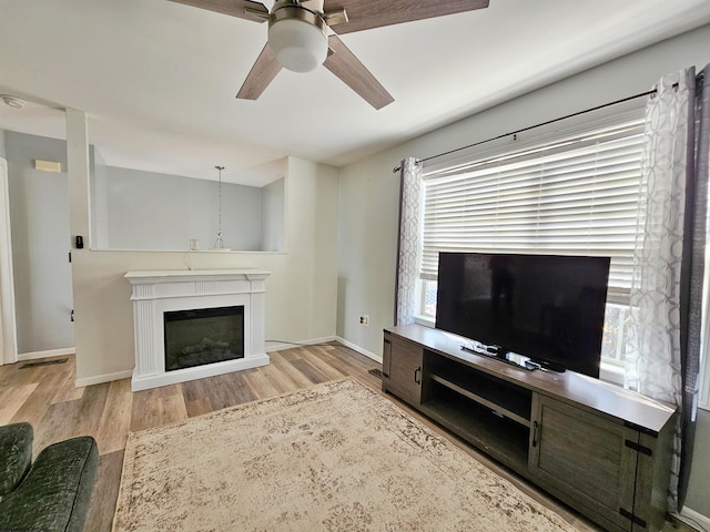 unfurnished living room with baseboards, a ceiling fan, a glass covered fireplace, wood finished floors, and a healthy amount of sunlight