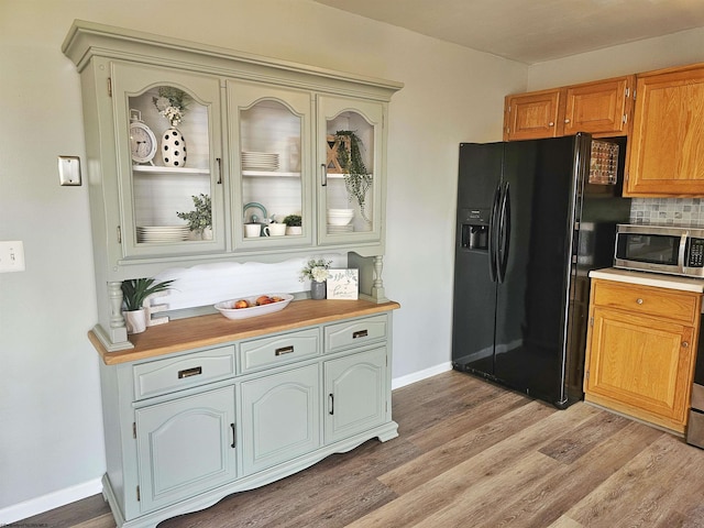 kitchen featuring light wood finished floors, stainless steel microwave, light countertops, and black fridge with ice dispenser