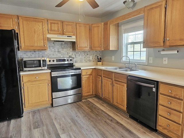 kitchen featuring under cabinet range hood, a sink, light countertops, appliances with stainless steel finishes, and light wood finished floors