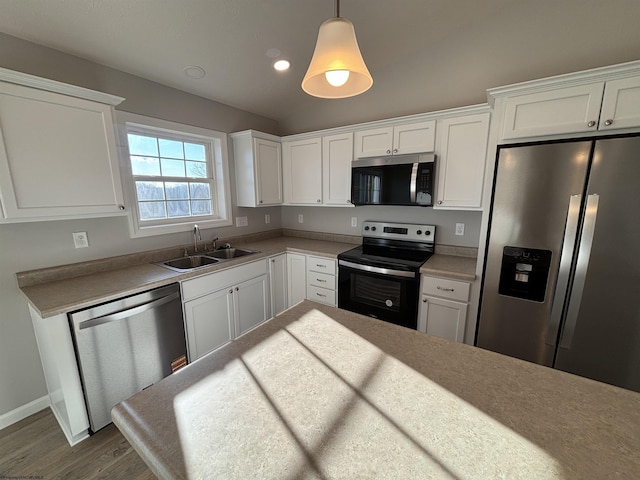 kitchen with white cabinets, lofted ceiling, appliances with stainless steel finishes, hanging light fixtures, and a sink