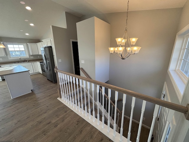 stairs with an inviting chandelier, vaulted ceiling, wood finished floors, and recessed lighting