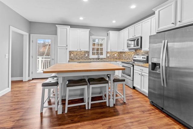 kitchen with white cabinets, stainless steel appliances, a kitchen bar, wooden counters, and a sink