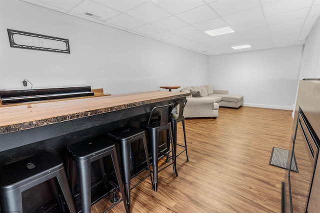 interior space featuring a paneled ceiling, baseboards, a dry bar, and light wood finished floors