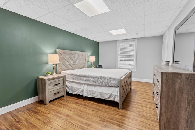 bedroom with light wood-type flooring, a paneled ceiling, and baseboards