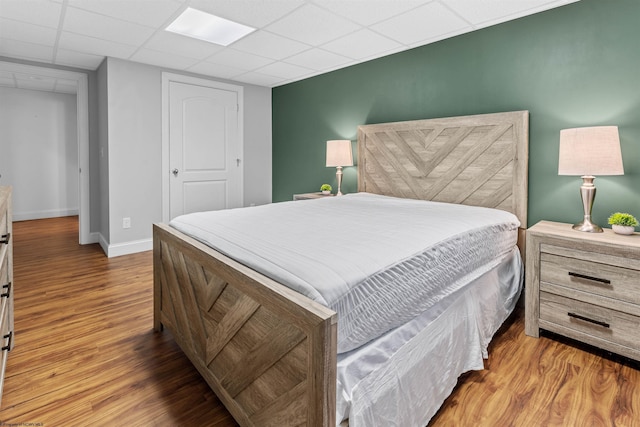 bedroom with a paneled ceiling, baseboards, and wood finished floors