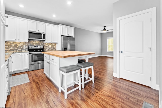 kitchen featuring a breakfast bar, stainless steel appliances, visible vents, white cabinets, and butcher block countertops