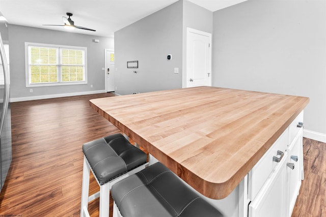 kitchen featuring ceiling fan, baseboards, white cabinets, a center island, and dark wood-style floors