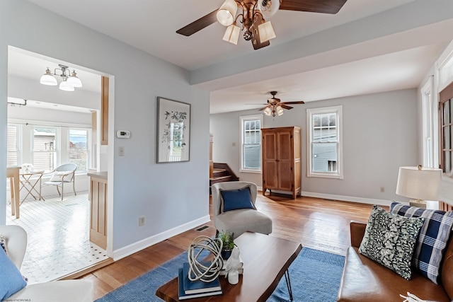 living room with stairway, baseboards, wood finished floors, and ceiling fan with notable chandelier