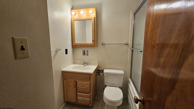 bathroom featuring toilet, bath / shower combo with glass door, vanity, and baseboards