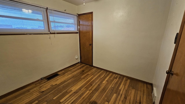 empty room featuring dark wood-style flooring, visible vents, and baseboards