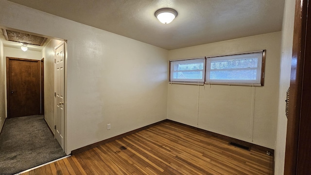 empty room featuring attic access, visible vents, dark wood finished floors, and baseboards