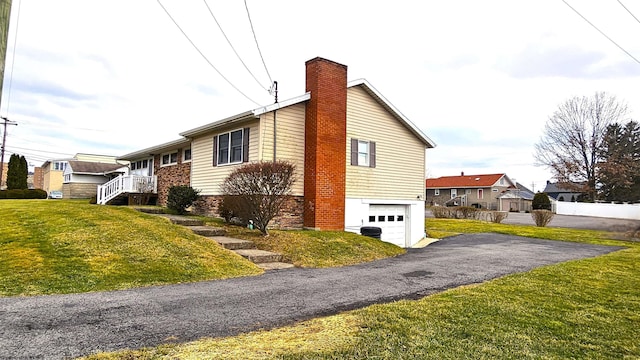 view of side of property with driveway, a yard, a chimney, and an attached garage